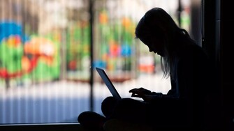 a student is silhouetted sitting on the floor with a laptop.